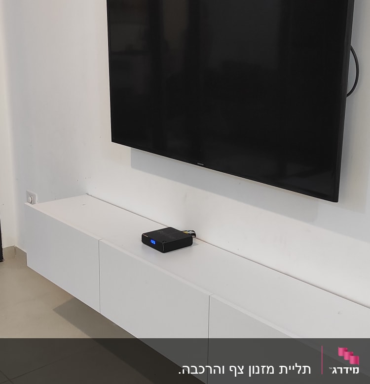 טלוויזיה תלויה על קיר מעל ארונית לבנה